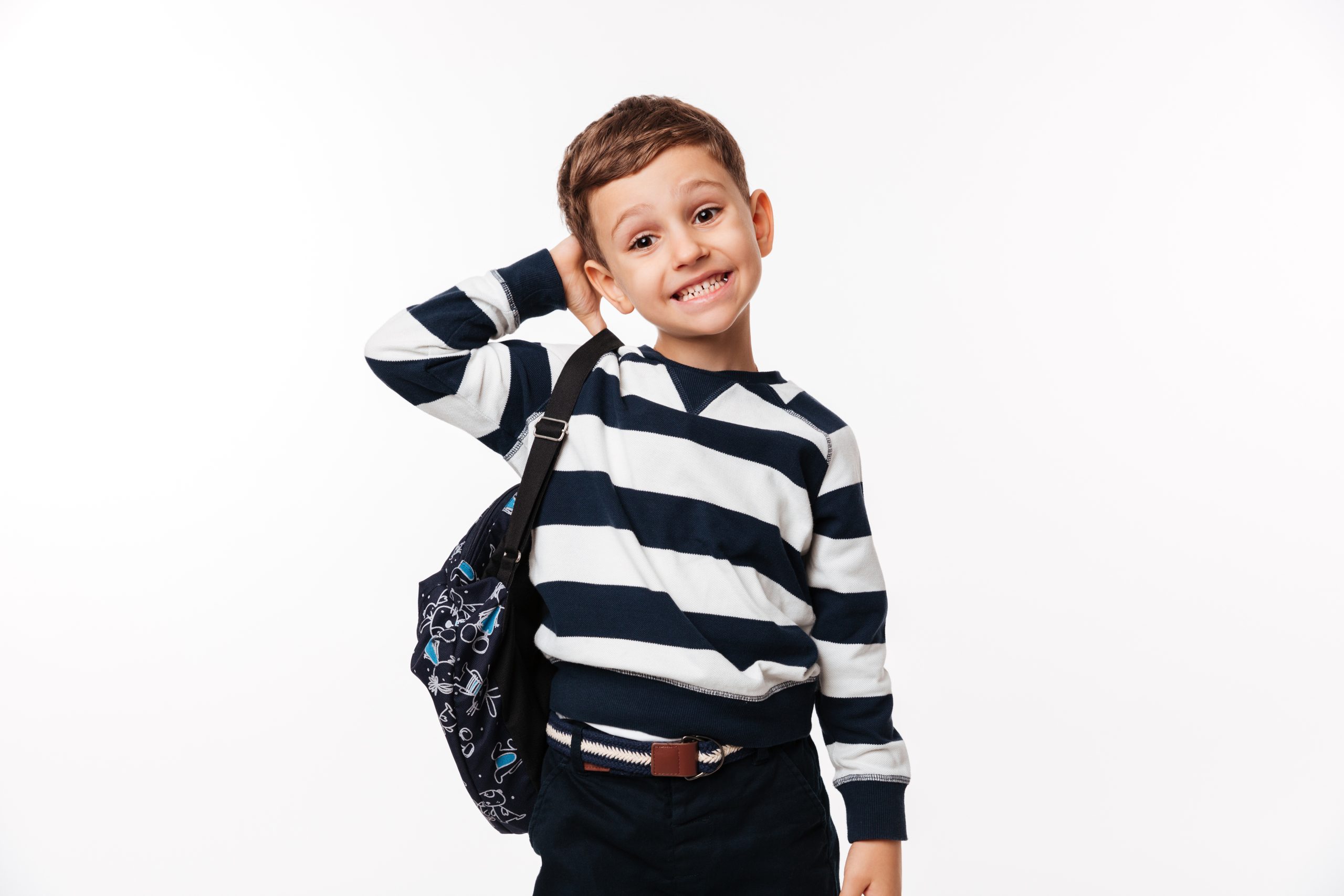 Portrait of a confused cute little kid with backpack scratching his head and looking at camera isolated over white background